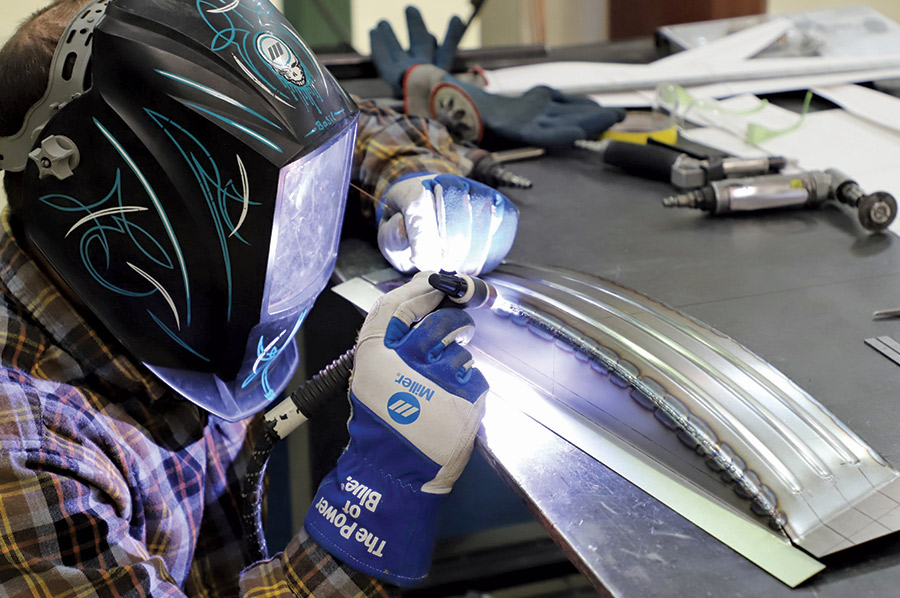 person wearing a welding helmet working on a piece of the sheetmetal cover