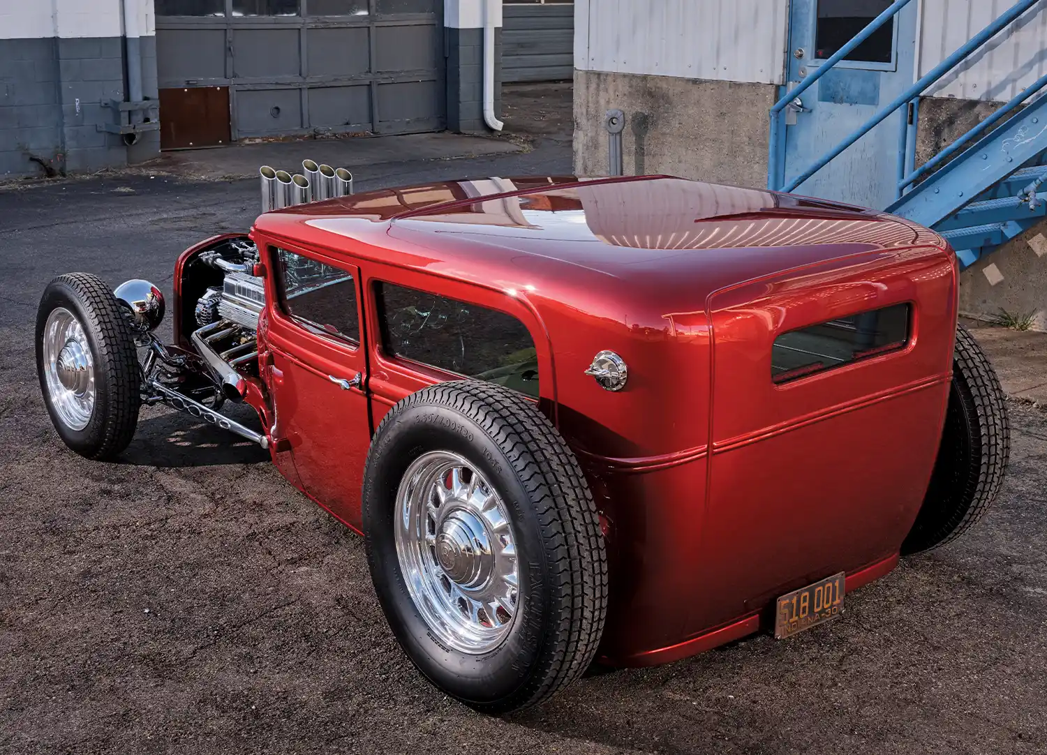 Close-up rear view of the 1930 Ford Model A Hot Rod, featuring its wide rear tires and custom bodywork under a blue staircase