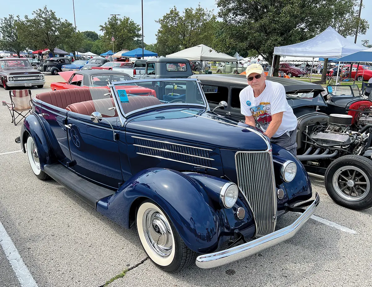 A proud owner poses with his navy blue 1936 Ford Cabriolet convertible at the 2024 Street Rod Nationals