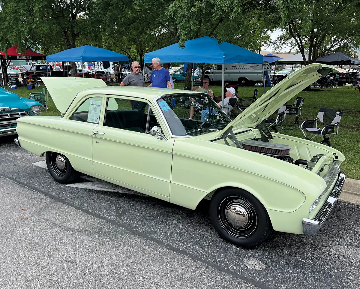 A light green 1962 Ford Falcon with its hood open, showcasing its clean engine bay at the show