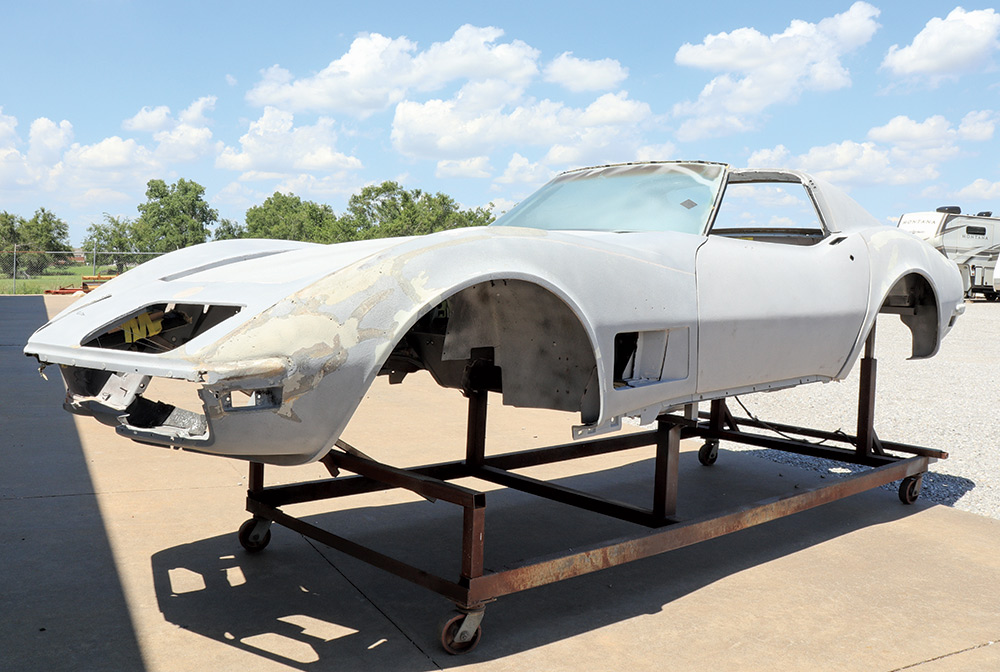 Chevrolet Corvette's fiberglass work exposed while sitting on a rolling metal frame in a sunny outdoor area