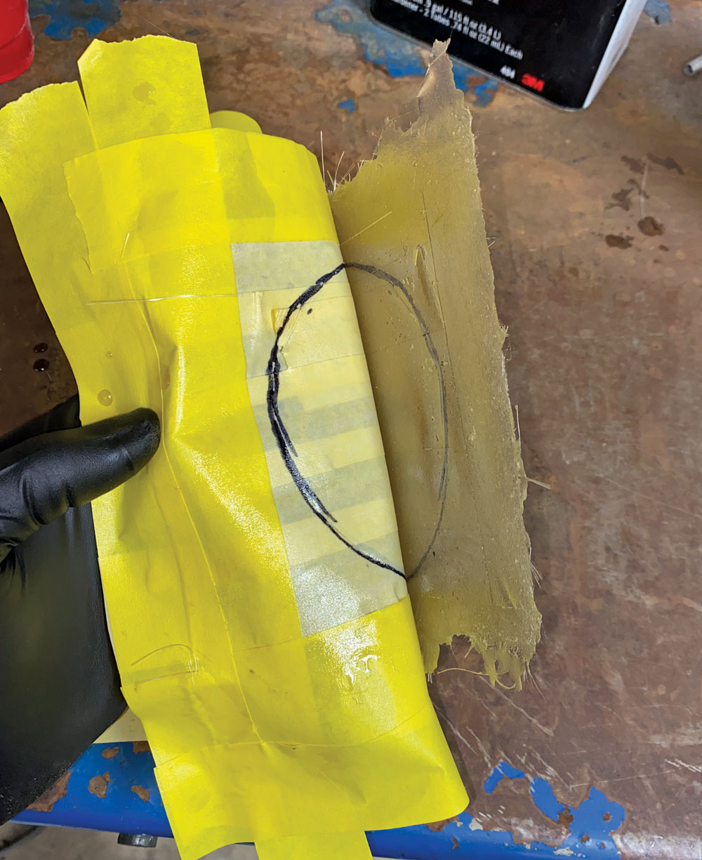hand wearing glove peeling yellow masking tape template off of fiberglass 