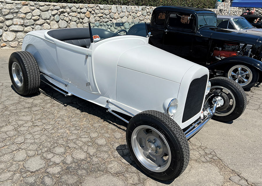 A sleek white 1929 Ford Model A roadster with modernized wheels parked on a street