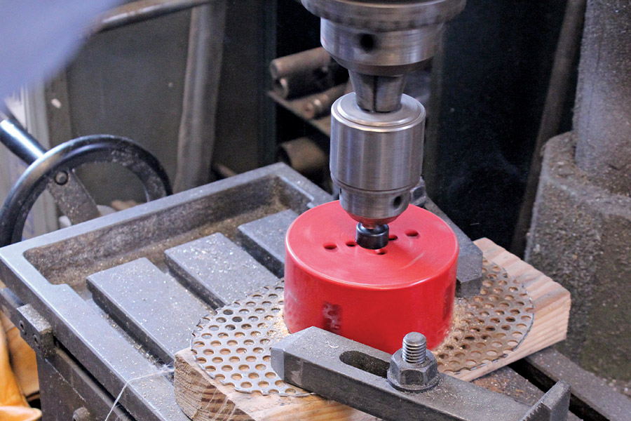 Red hole saw in use on a drill press for precise metalwork