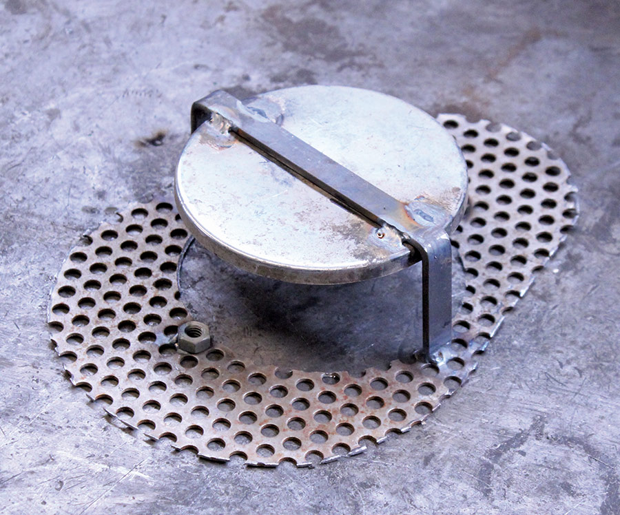 A metal air filter cover in progress, mounted on a perforated backing plate during the restoration process