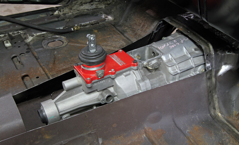 A car transmission with a red component labeled "TREMEC" installed in a rusted vehicle chassis.