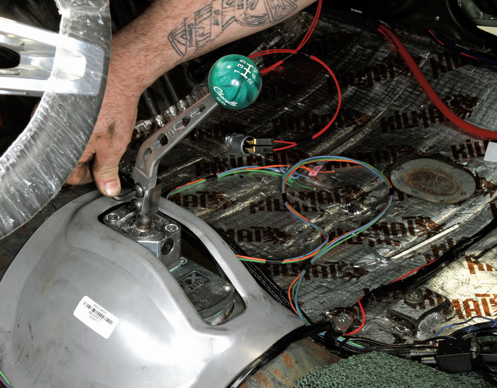 Person adjusting a car gear shifter amid multicolored wires and "KILMAT" soundproofing.
