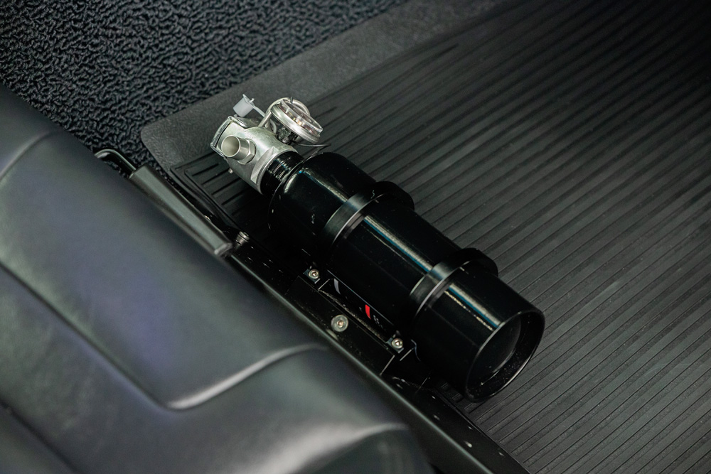 Close-up of a black cylinder with metallic fixtures on a ridged surface inside a vehicle.