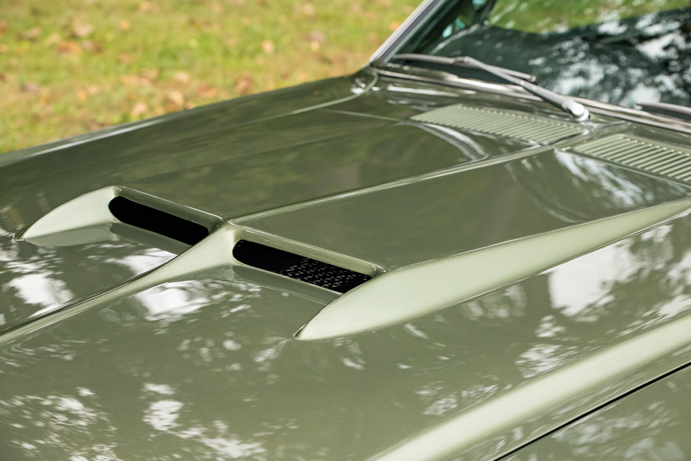 Metallic green car hood with two air scoops reflecting trees.