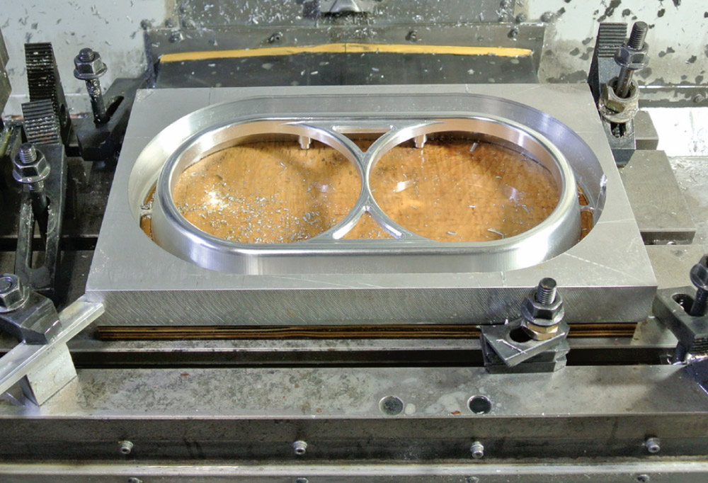 machined aluminum headlight bezel in progress for a 1959 Chevy Impala, secured on a CNC milling machine