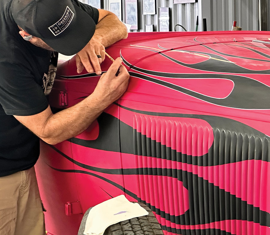 Artist adding white pinstriping details to outline black flames on the roadster's pink body
