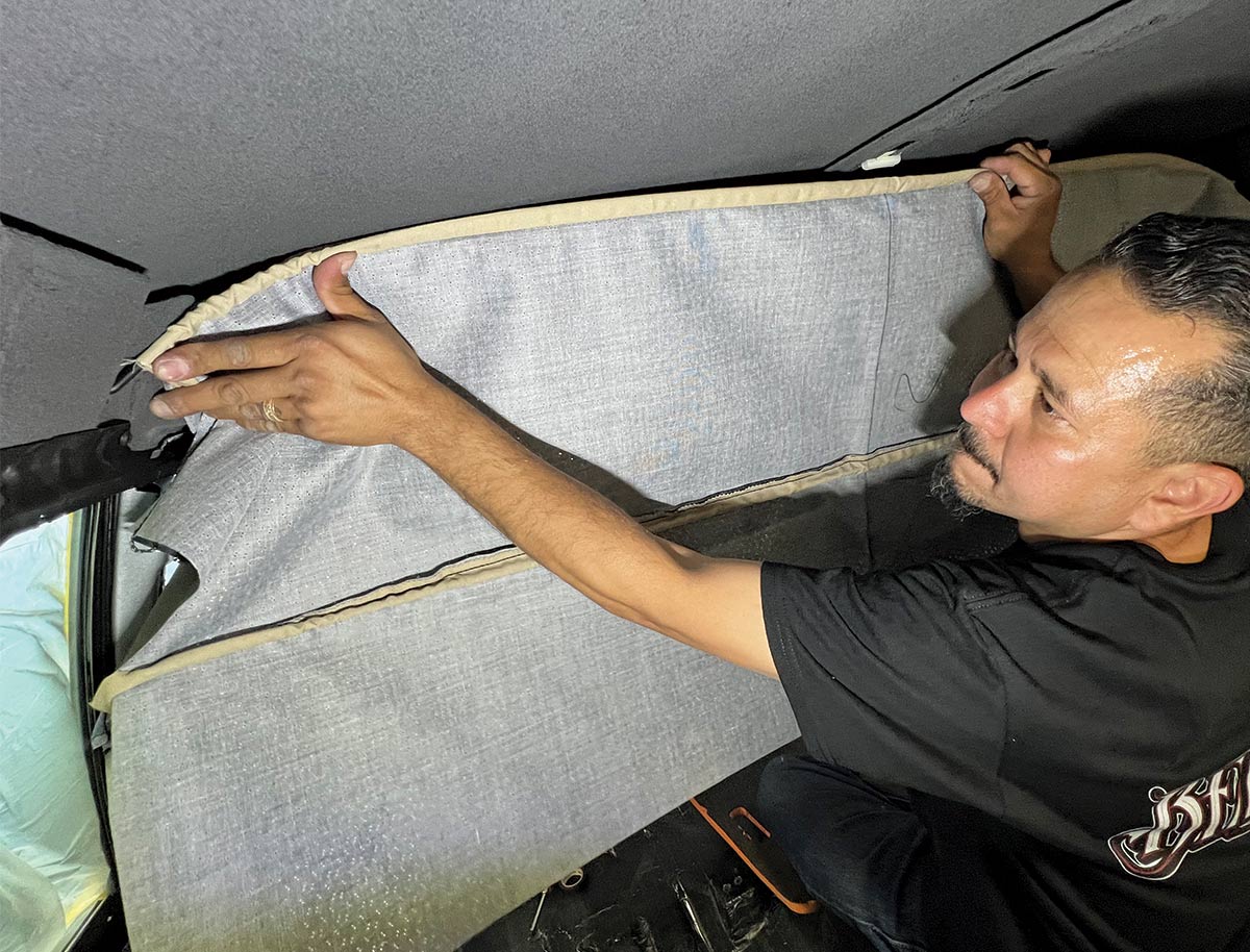 Worker stretching and fitting the headliner fabric into place inside a 1970 Chevy Nova