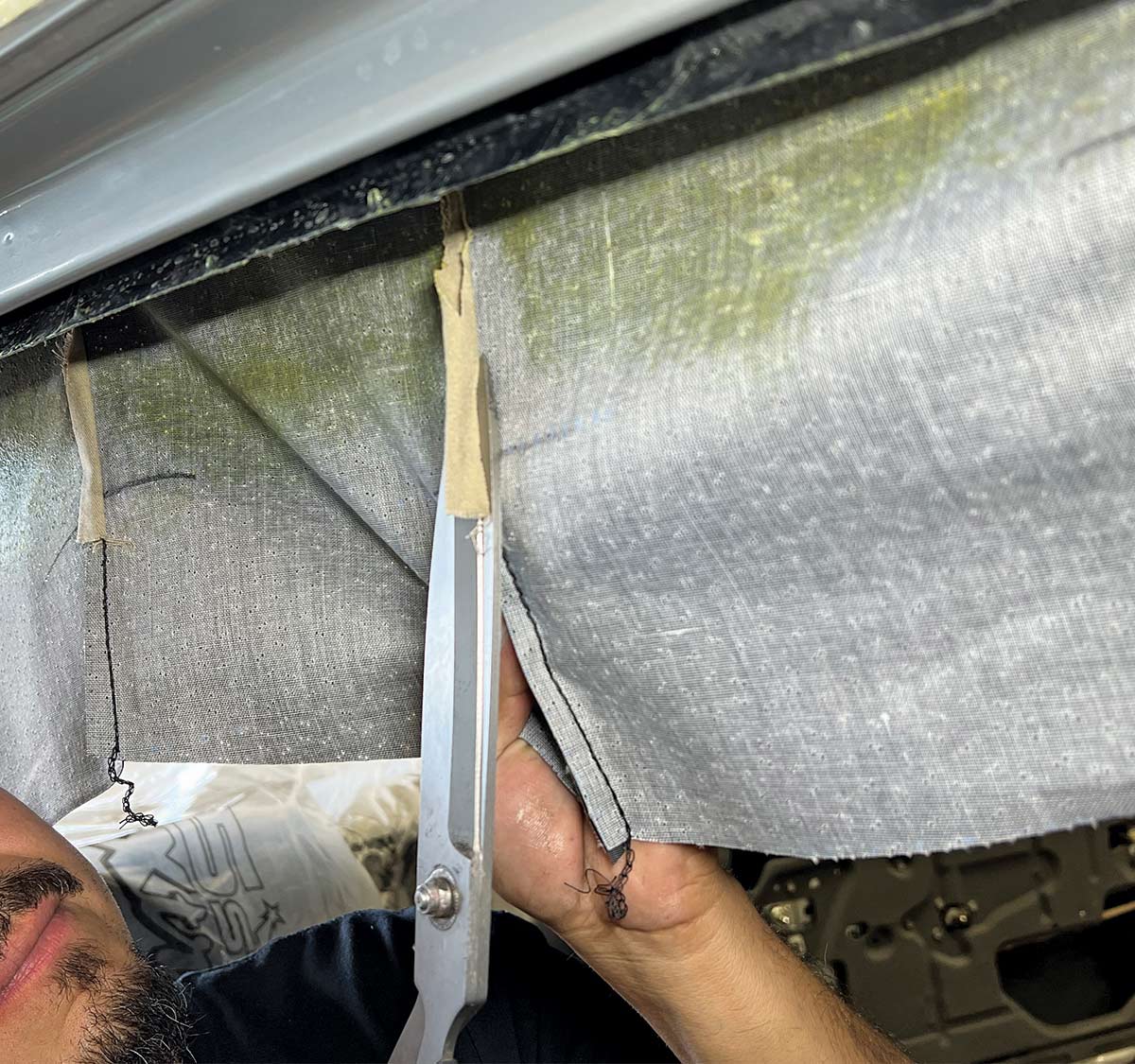 Cutting the headliner material near the edges for proper installation in a 1970 Chevy Nova