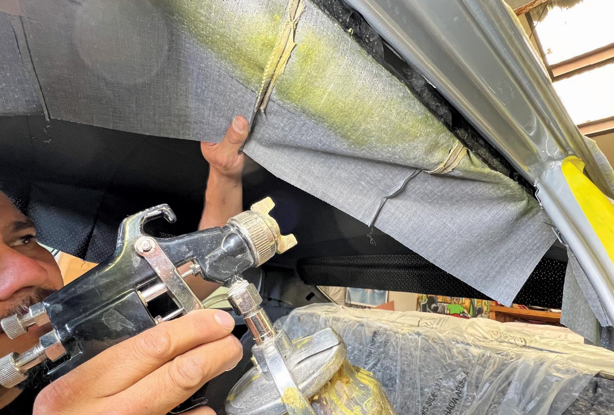 Applying adhesive to secure the headliner fabric inside a 1970 Chevy Nova