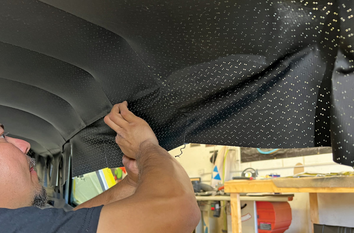 Worker stretching and fitting the headliner for a clean finish in a 1970 Chevy Nova