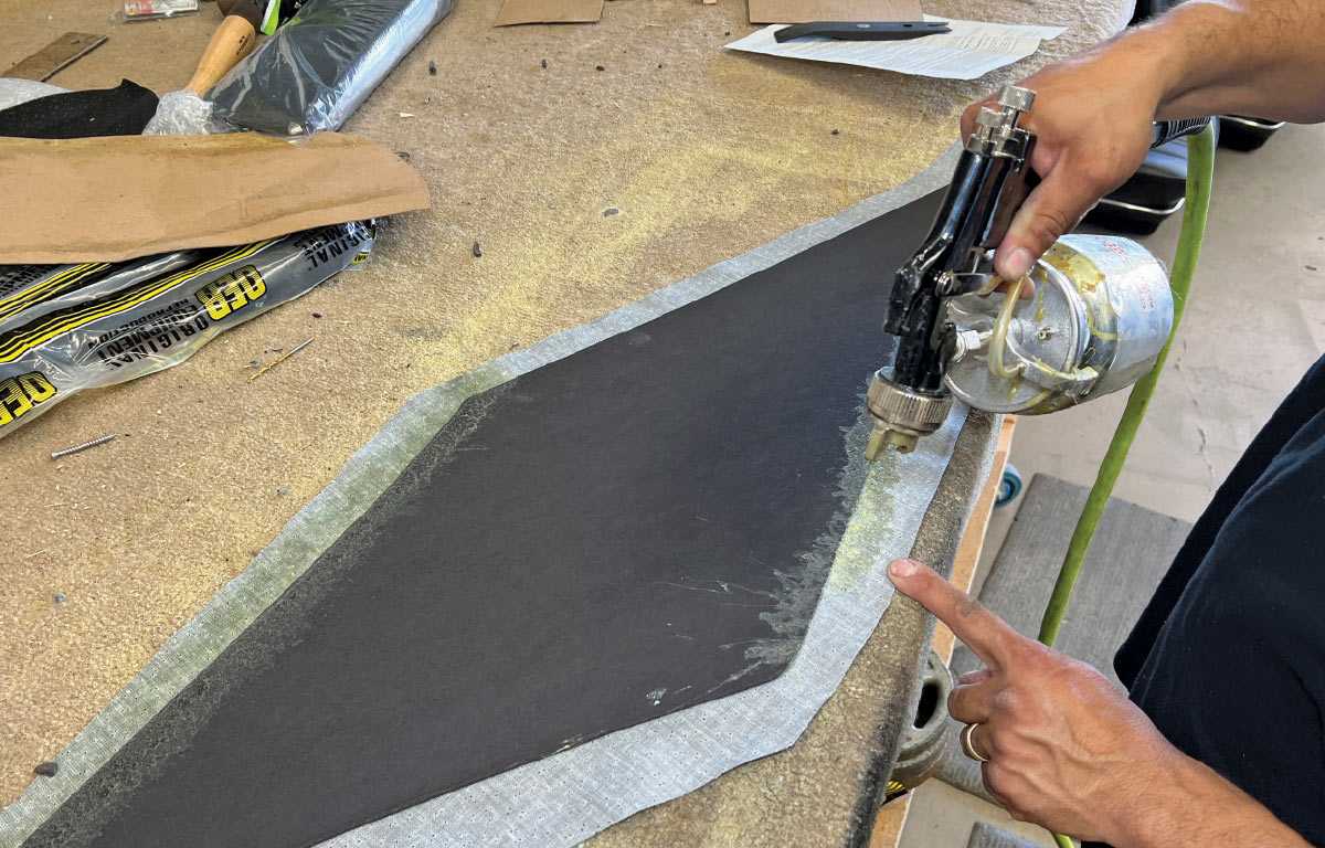 Spraying adhesive onto a trim panel for final upholstery touches in a 1970 Chevy Nova