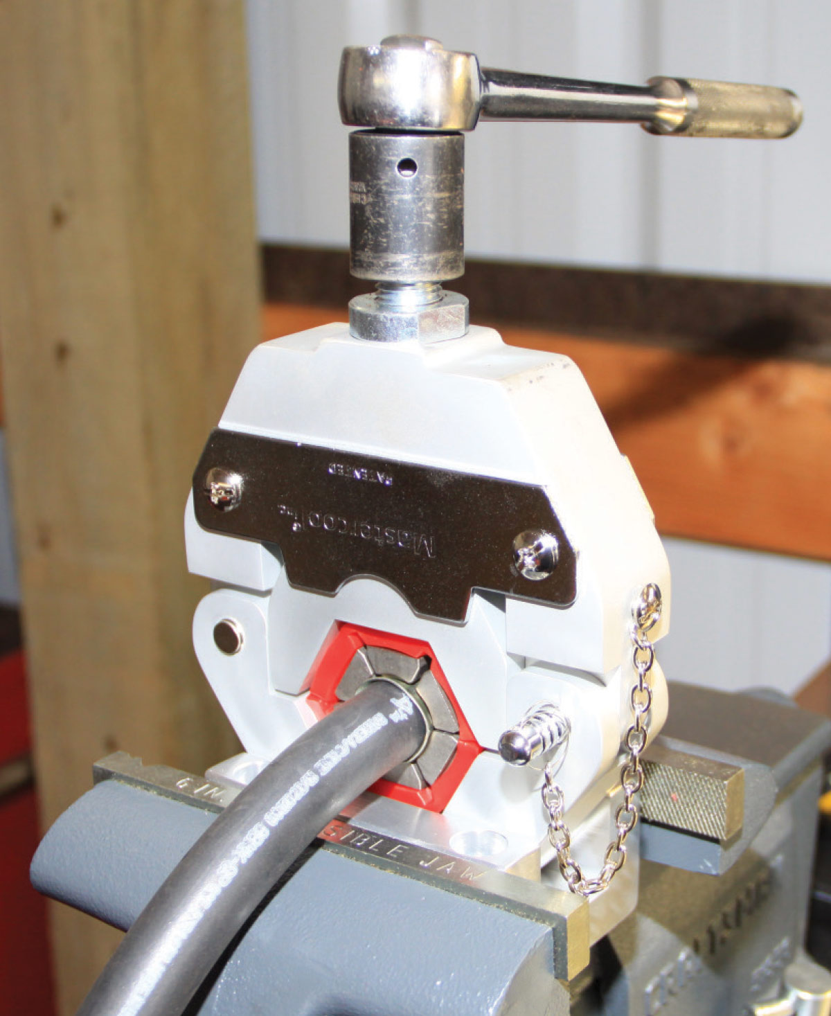 A hydraulic crimping tool securing an AC hose fitting in a vise for proper installation