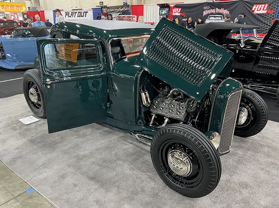 Deep green 1932 Ford Tudor hot rod with a louvered hood, black steel wheels, and a flathead V8 engine