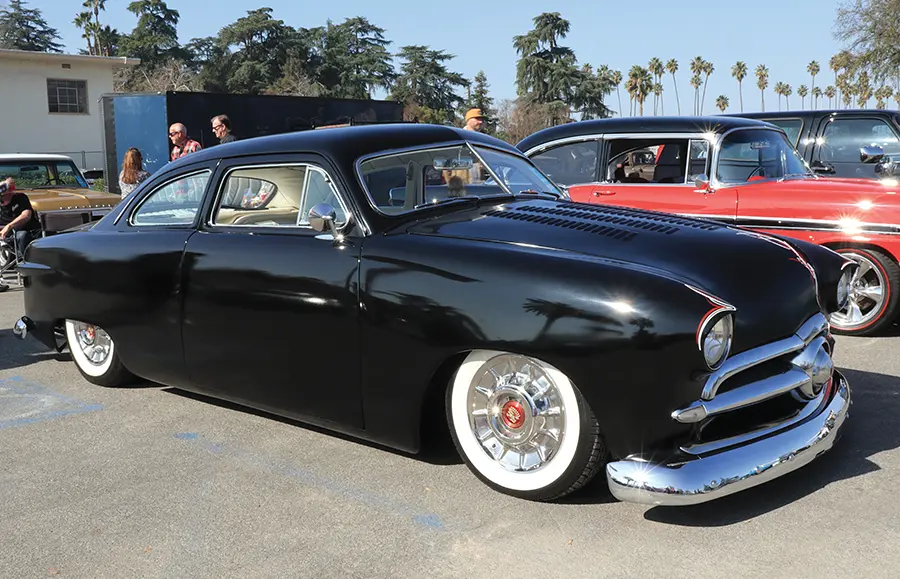 Glossy black 1950 Ford coupe with white-wall tires, a chopped roof, and a custom grille