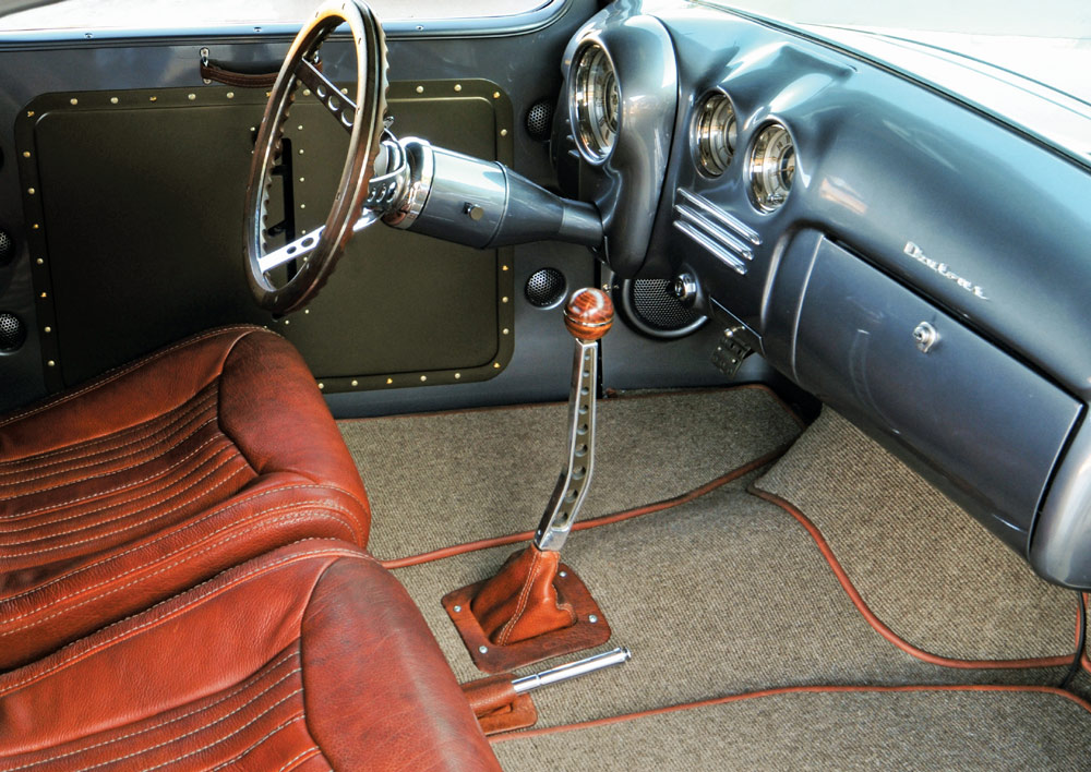 Interior of a vintage car with brown leather seats, a blue dashboard, and classic steering and gear shift design.