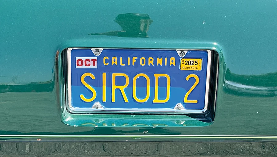 Close-up of a California license plate with "SIROD 2" vanity lettering, mounted on a green vintage hot rod. The plate has an October 2025 sticker.