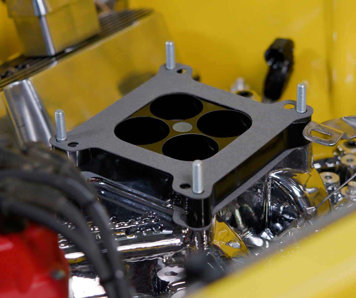 Close-up of 4-hole spacer plate installed on Edelbrock intake with stainless hardware