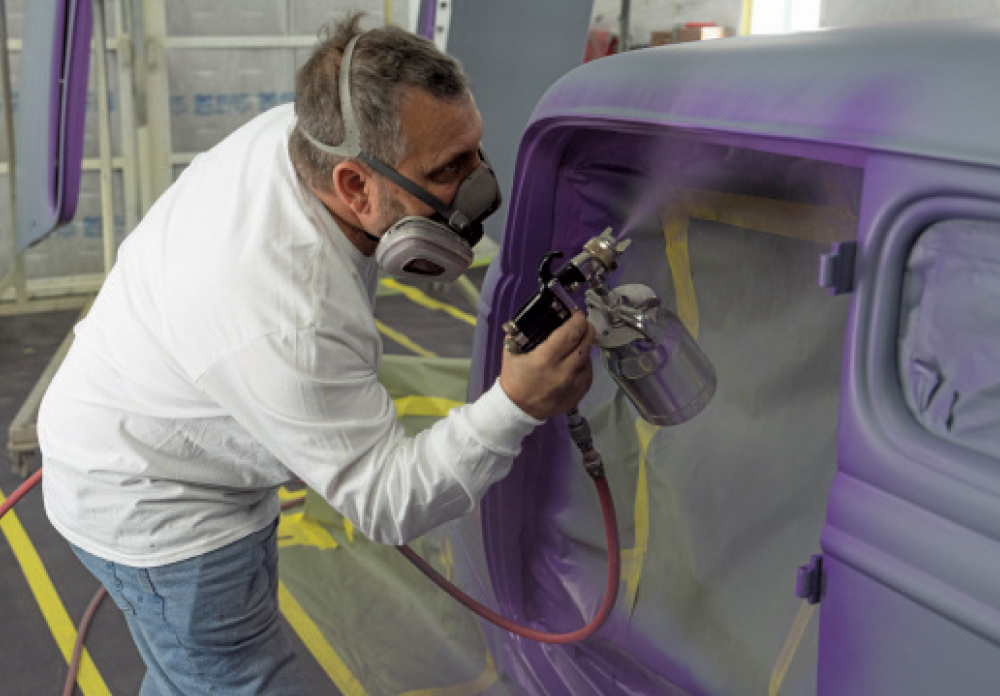 Technician applying metallic purple paint to 1930s Ford coupe in booth