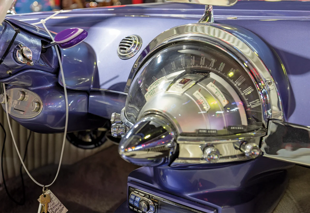 Close-up of a custom car dashboard with a large, chrome-rimmed speedometer gauge and a modern digital stereo receiver mounted below