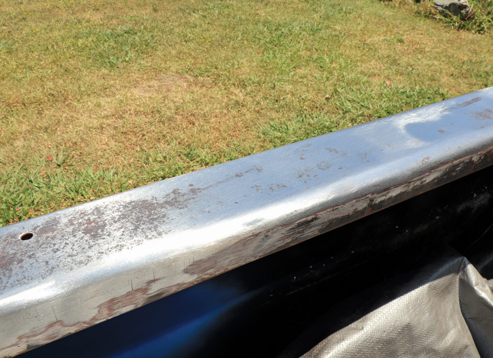 A close-up of the bed rail of the pickup truck after sanding, showing the clean, bare silver metal with patches of surface rust remaining.