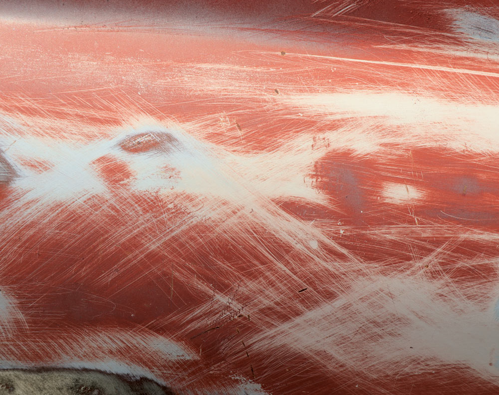 A close-up of the truck's body panel covered in distinct, sweeping sanding marks, revealing red paint, white primer, and light bare metal streaks.