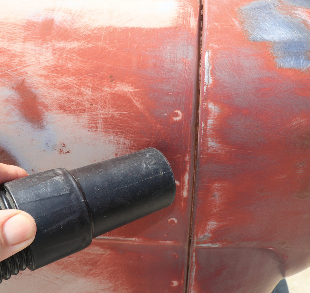 A hand uses a vacuum hose attachment to clean sanding dust and debris from a seam between two body panels on the truck.
