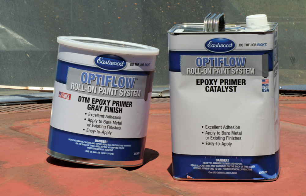 Two containers of Eastwood Optiflow Roll-on Paint System: the DTM Epoxy Primer Gray Finish and the Epoxy Primer Catalyst, sitting on a rusty surface.