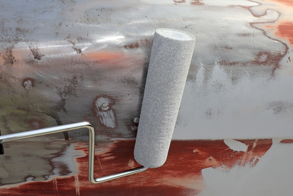 A gray paint roller applies the initial coat of primer to a section of the truck's body that has been sanded down to bare metal and old paint.