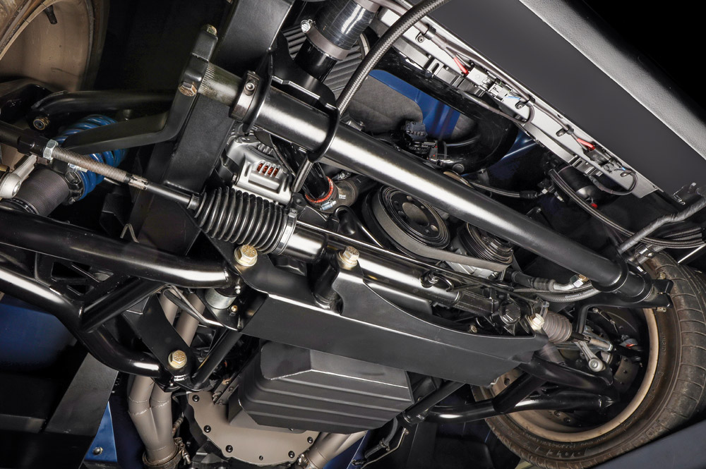 Underside shot of the car showing the clean, black-painted custom chassis, modern front-end suspension components, rack-and-pinion steering, and part of the exhaust system.