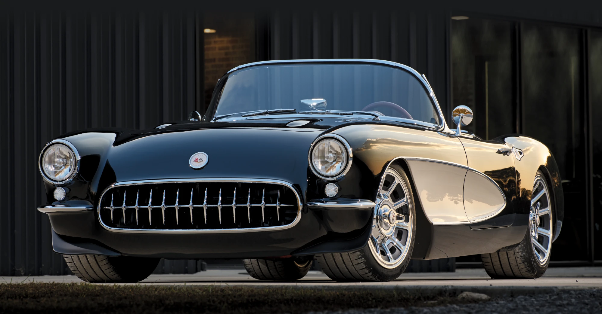 Front view of a shiny black classic Chevrolet Corvette convertible with chrome grille and modern custom chrome wheels.