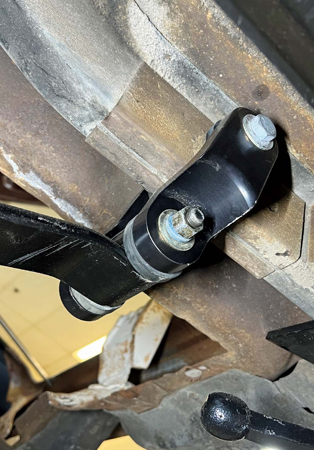 A vehicle undercarriage showing a black suspension link or control arm bolted to the frame with a urethane bushing.