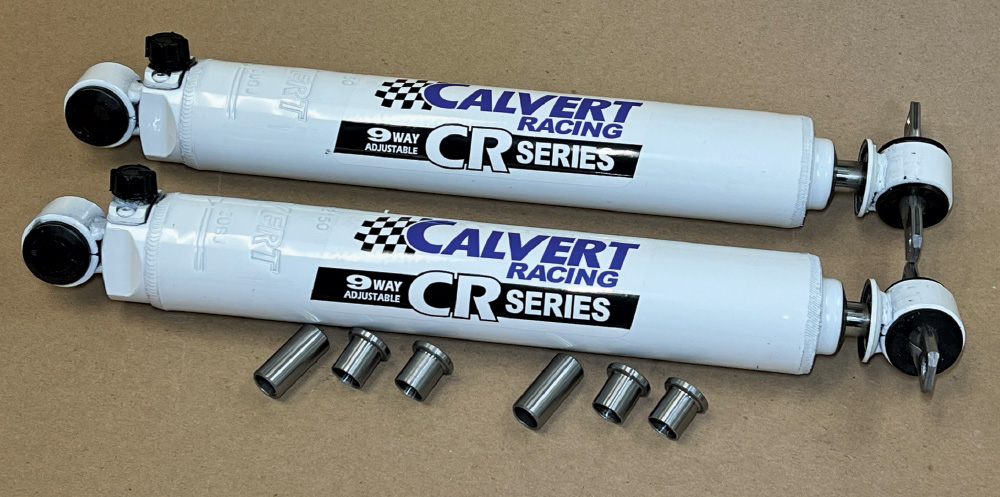 Two white Calvert Racing CR Series Adjustable shocks displayed on a surface alongside a set of metal mounting bushings.