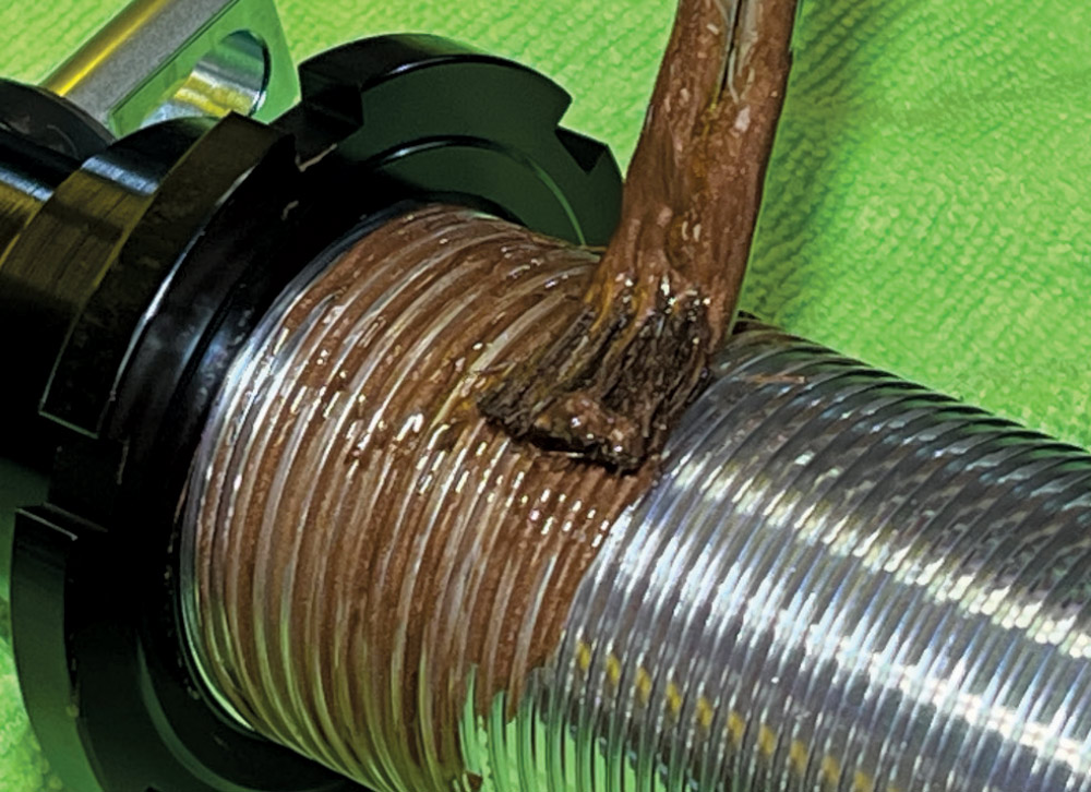 Close-up of a threaded coilover shock body where a brush is applying a thick layer of brown anti-seize compound to the threads.