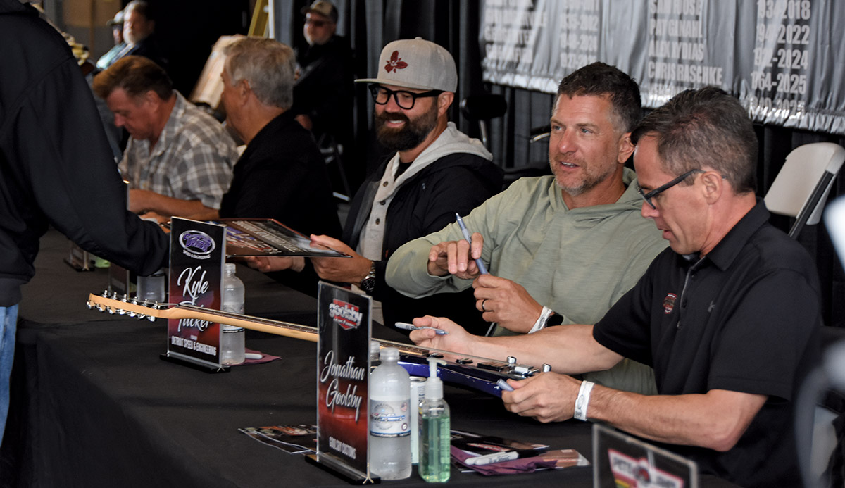 a group of men sit a table signing posters and guitars