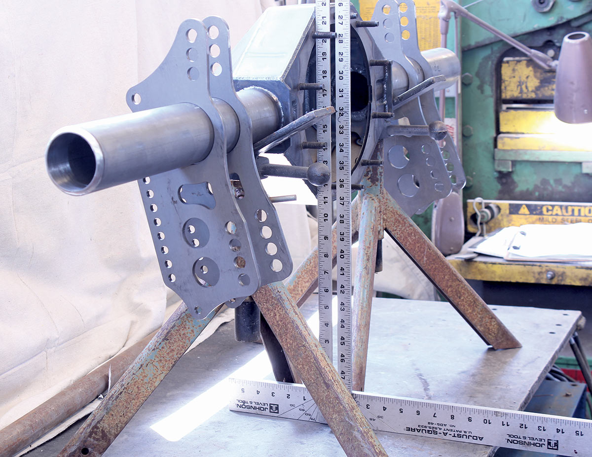 A custom rear-axle housing assembly held in a fabrication jig with measuring squares and a ruler for alignment.