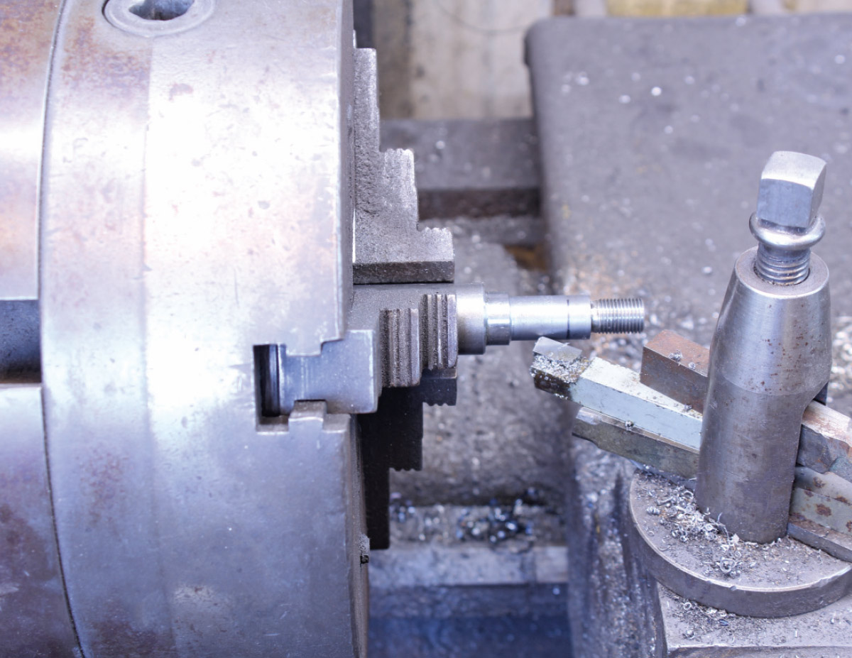 Close-up of a metal lathe machining a small steel part, with metal shavings scattered on the machine bed.
