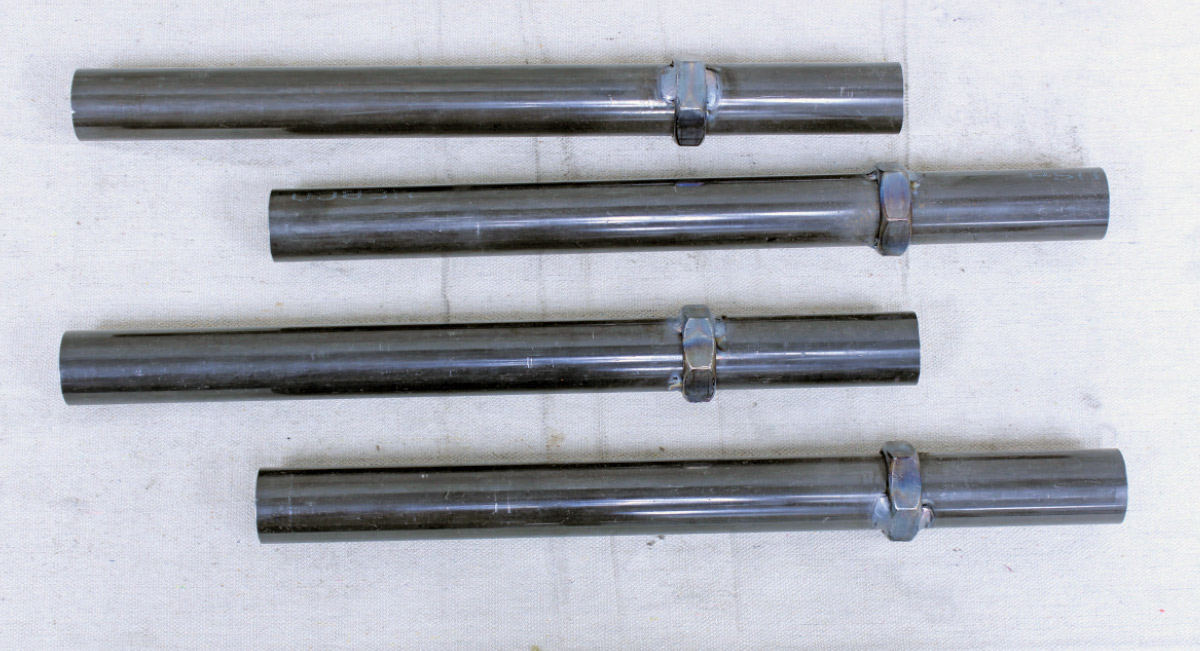 Four black steel suspension tubes with welded hex nuts arranged on a white cloth background.