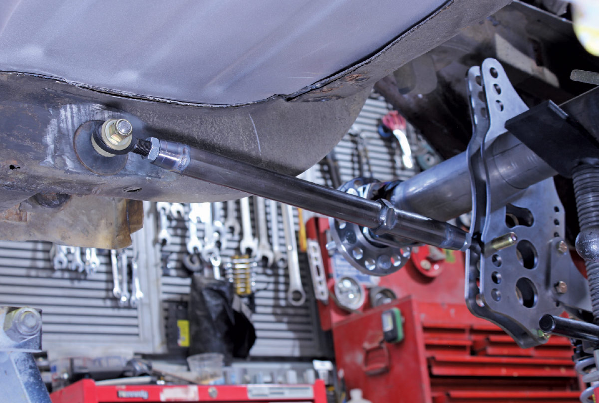 A suspension control arm with a rod end joint bolted to a mounting point on a vehicle's frame in a workshop.