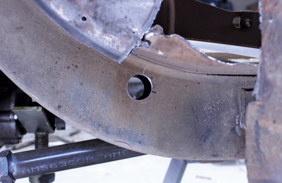 Close-up of a clean, circular hole drilled through the side of a curved metal vehicle frame rail.