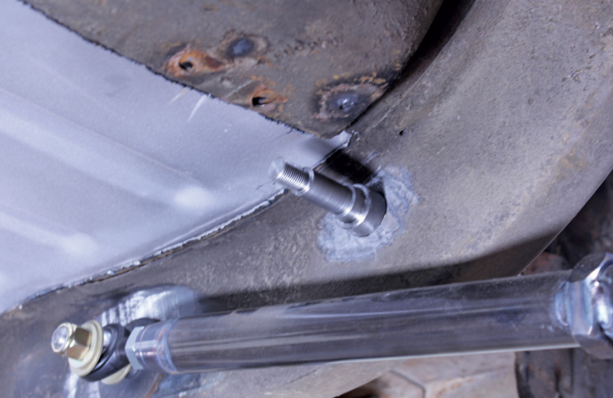 A threaded metal stud mounted into a vehicle frame rail, positioned above a suspension control arm.