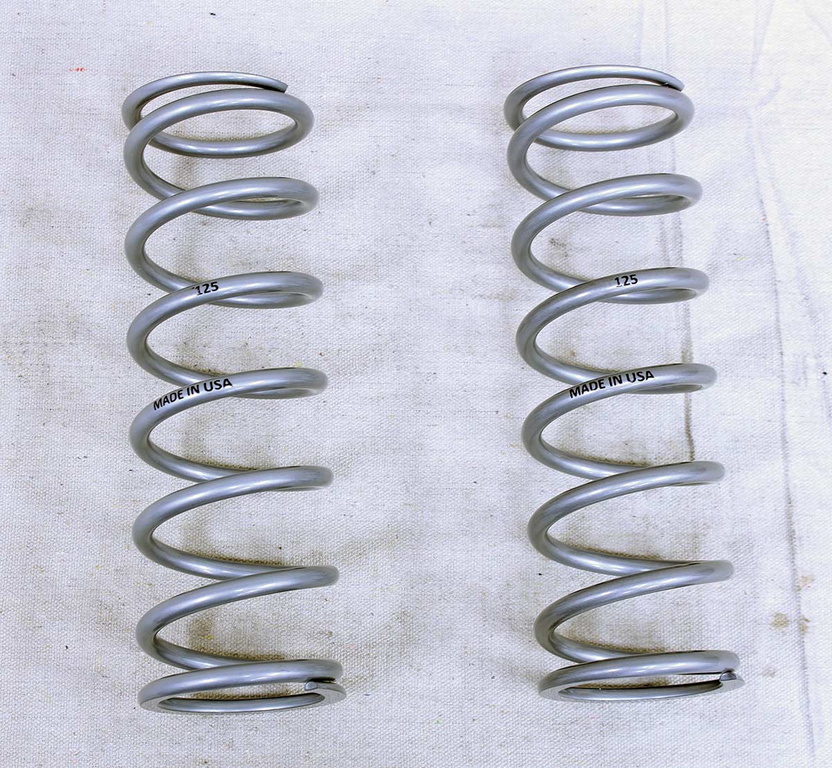 Two silver coil springs labeled "MADE IN USA" and "125" laid out vertically on a white cloth background.