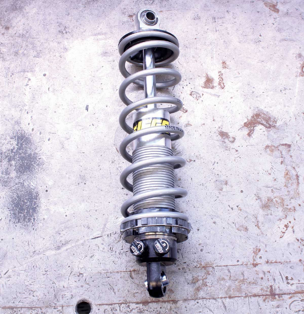A fully assembled silver JEGS coilover shock with the coil spring installed, shown on a workshop floor.