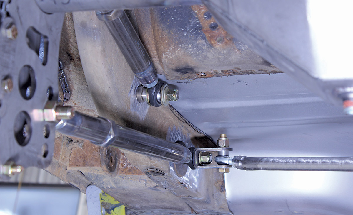 Close-up of suspension links and a rod end joint bolted to a mounting point on the underside of a vehicle.