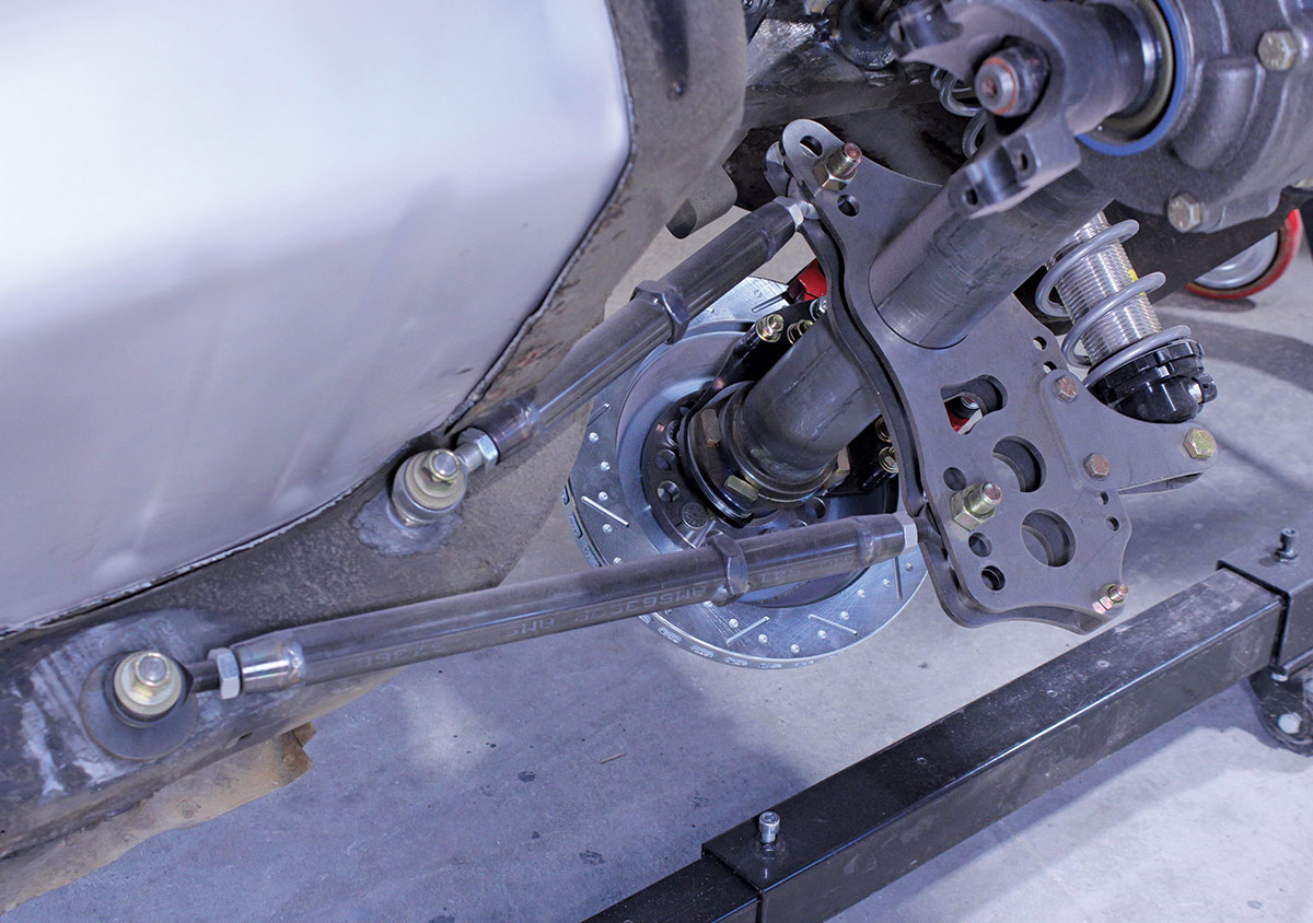 Detailed view of a suspension control arm and a cross-drilled disc brake rotor mounted on a custom axle assembly.