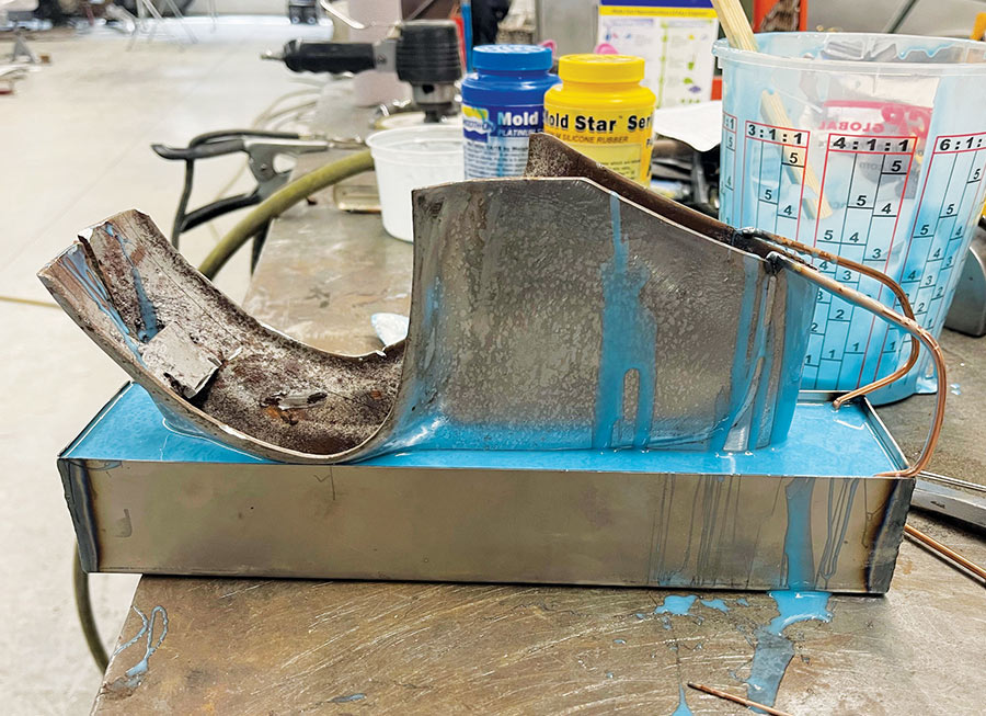 A custom-fabricated metal part being set into a tray of blue Mold Star silicone rubber for industrial mold making.